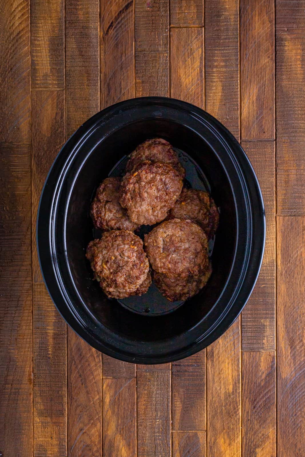 layered hamburger patties in an oval slow cooker.