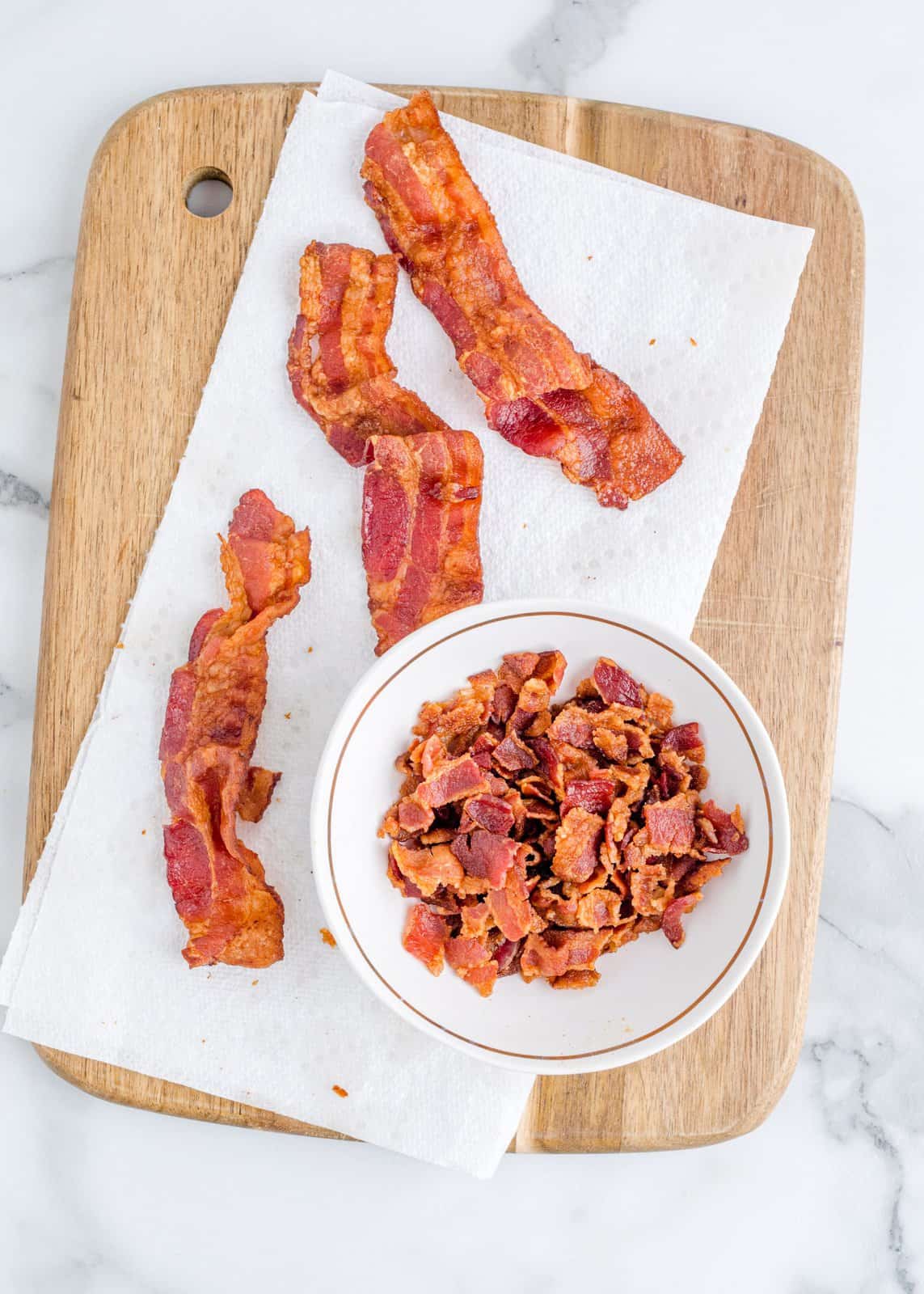 cooked bacon shown on a paper towel with some of the bacon shown crumbled in a bowl.