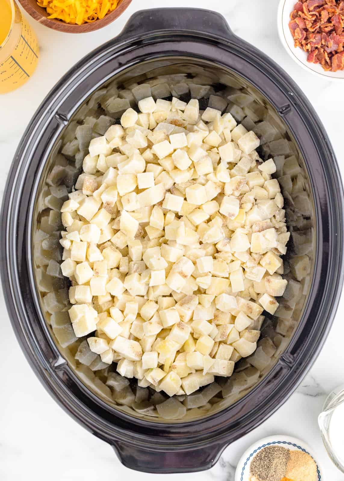 frozen hash brown cubes shown in the bottom of an oval slow cooker. 