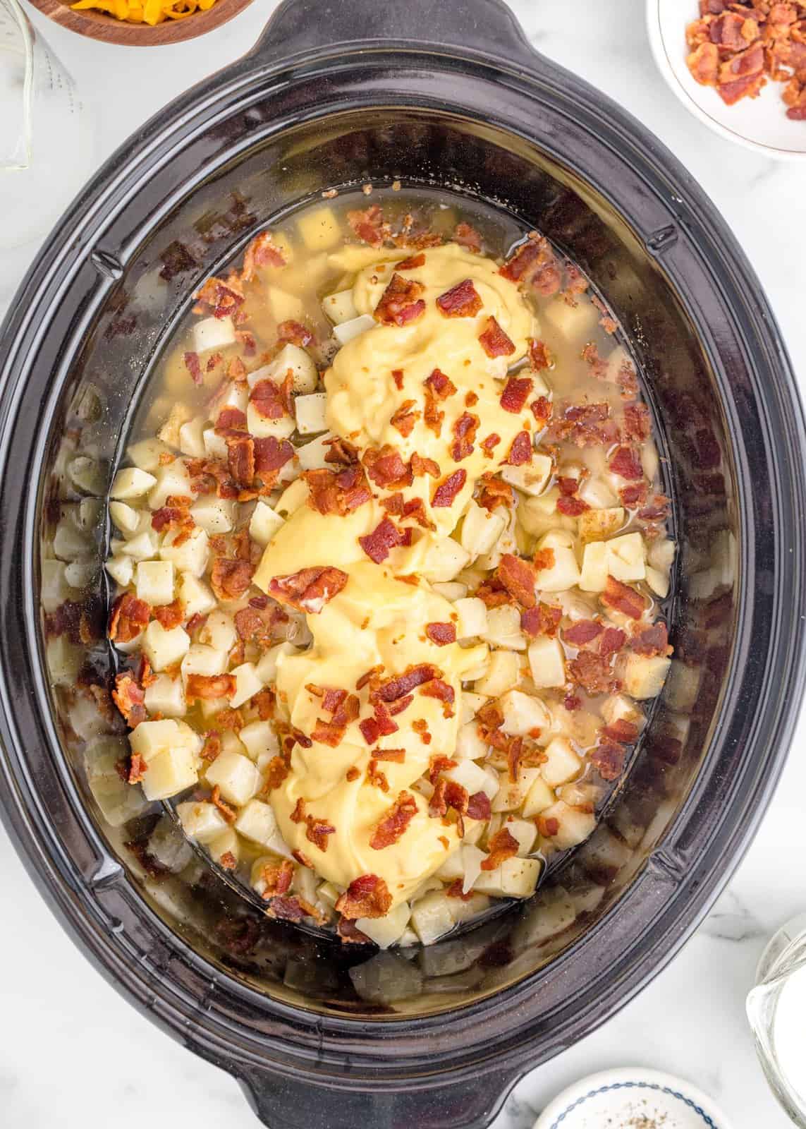 chicken broth, bacon and cream of chicken soup added to the oval slow cooker with the hash browns.