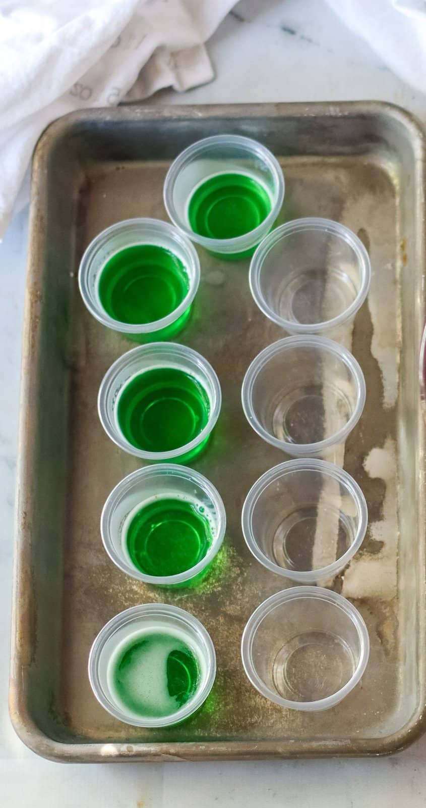 Green Jell-O being poured into plastic cups on tray.