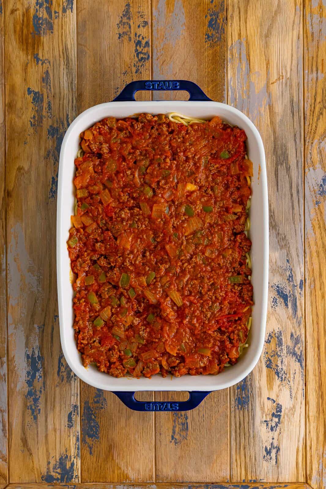 meat sauce spread evenly over spaghetti noodles in a casserole dish.