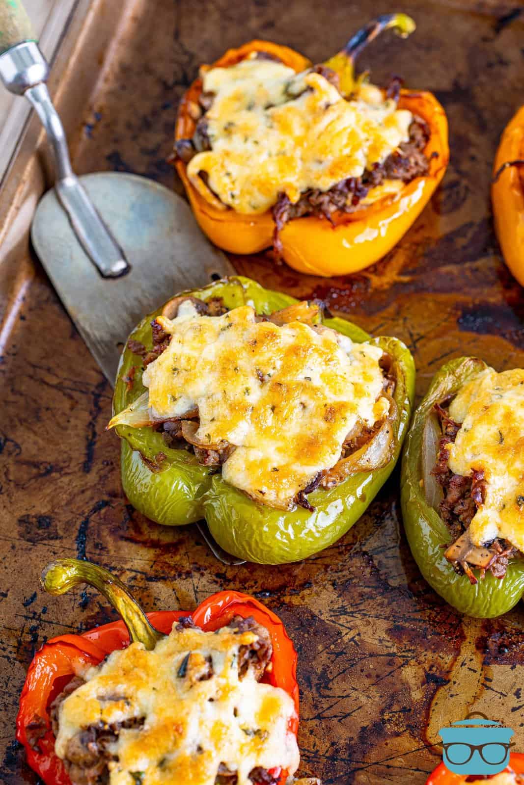 fully baked cheesesteak stuffed peppers on a baking sheet with a spatula scooping out one of the green peppers on the tray.