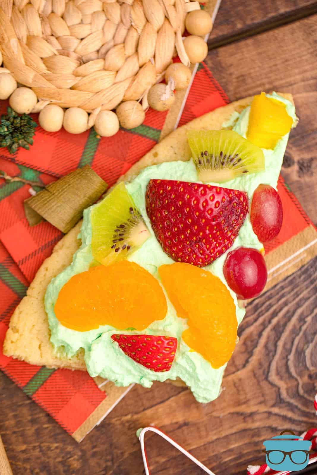 Slice cut off of the Christmas Tree Fruit Pizza on holiday napkin.