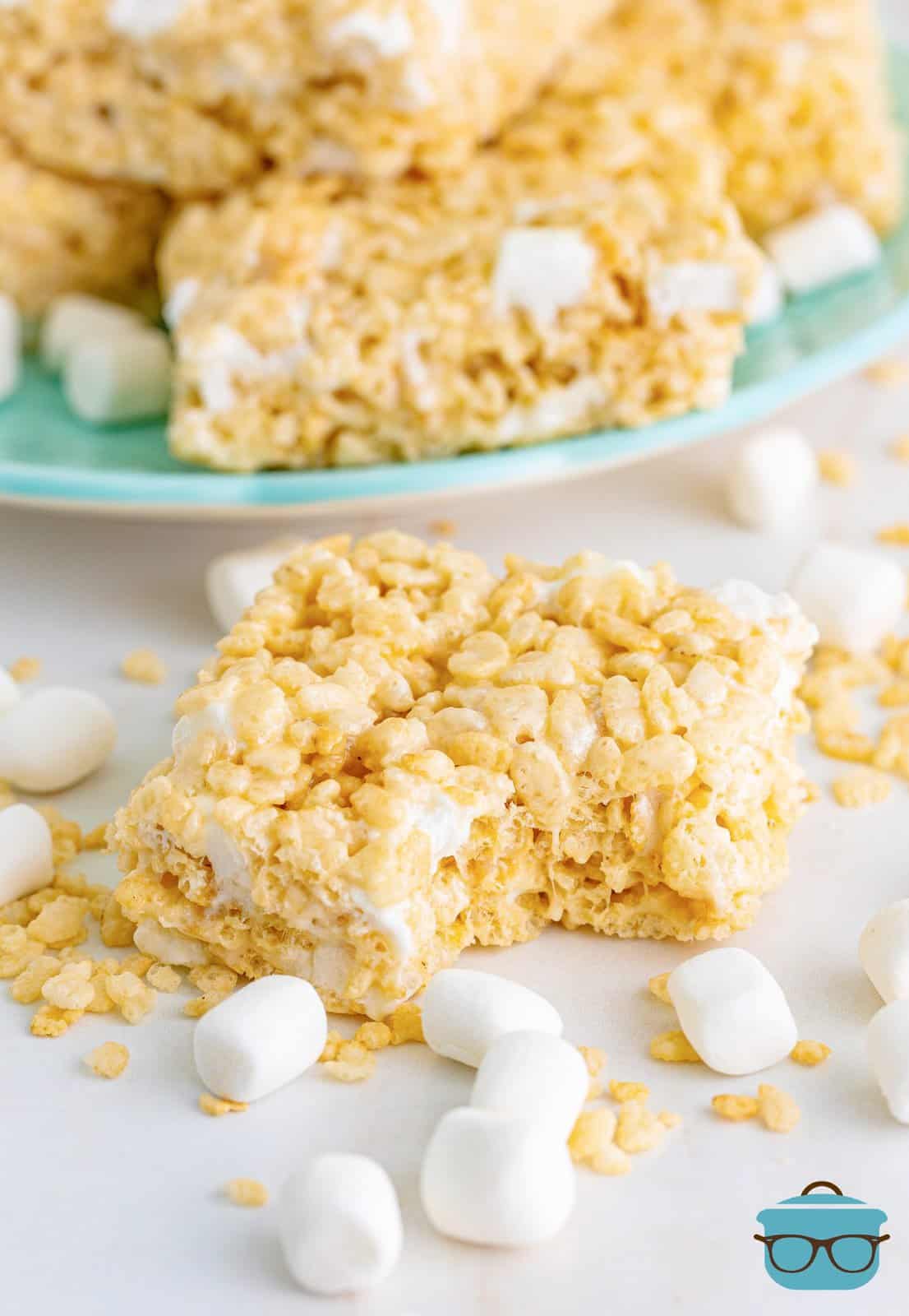 A rice krispie treat with a bite taken out of it and mini marshmallows around it.