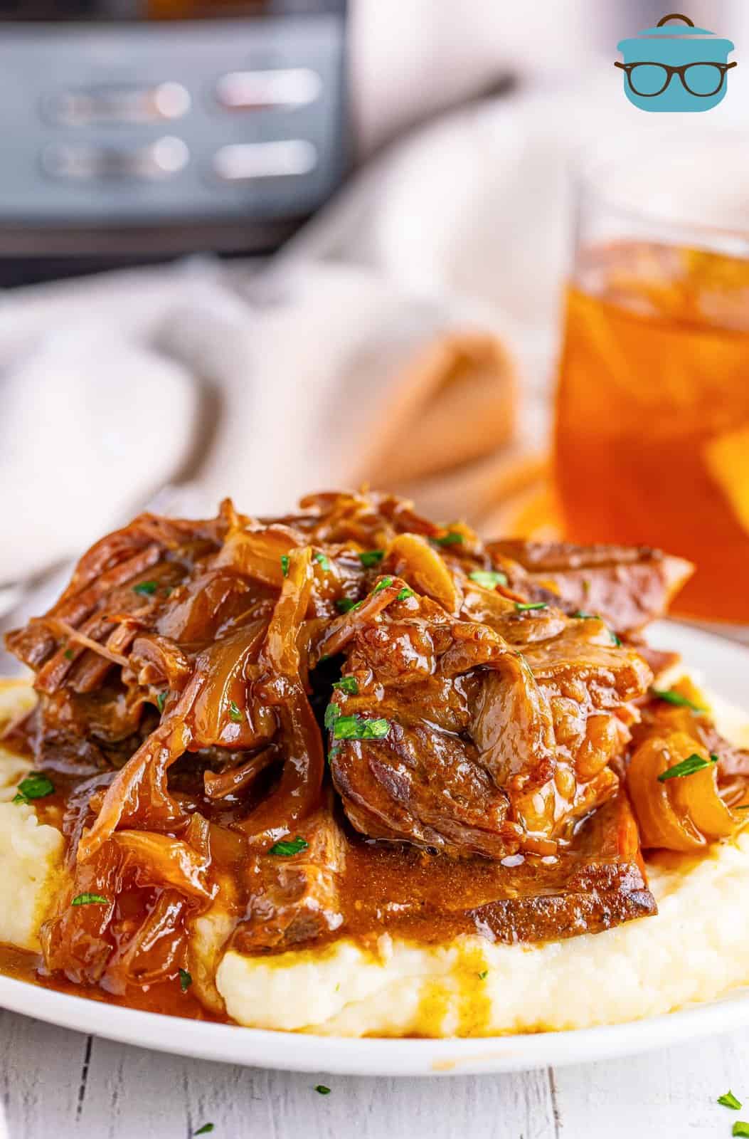 A serving of Slow Cooker French Onion Pot Roast over a bed of mashed potatoes on a plate.