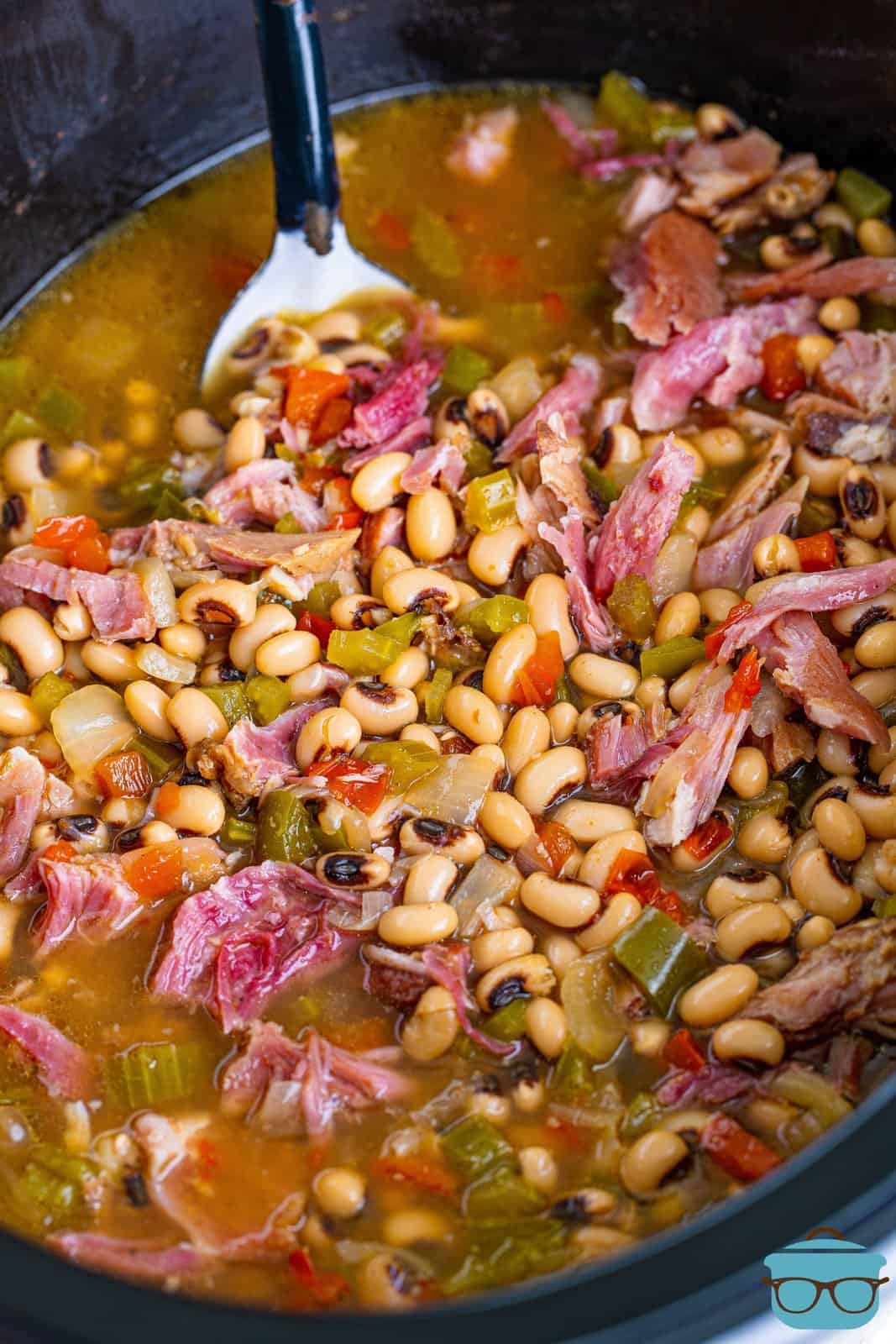 a large spoon inserted into cooked black eyed peas and ham.
