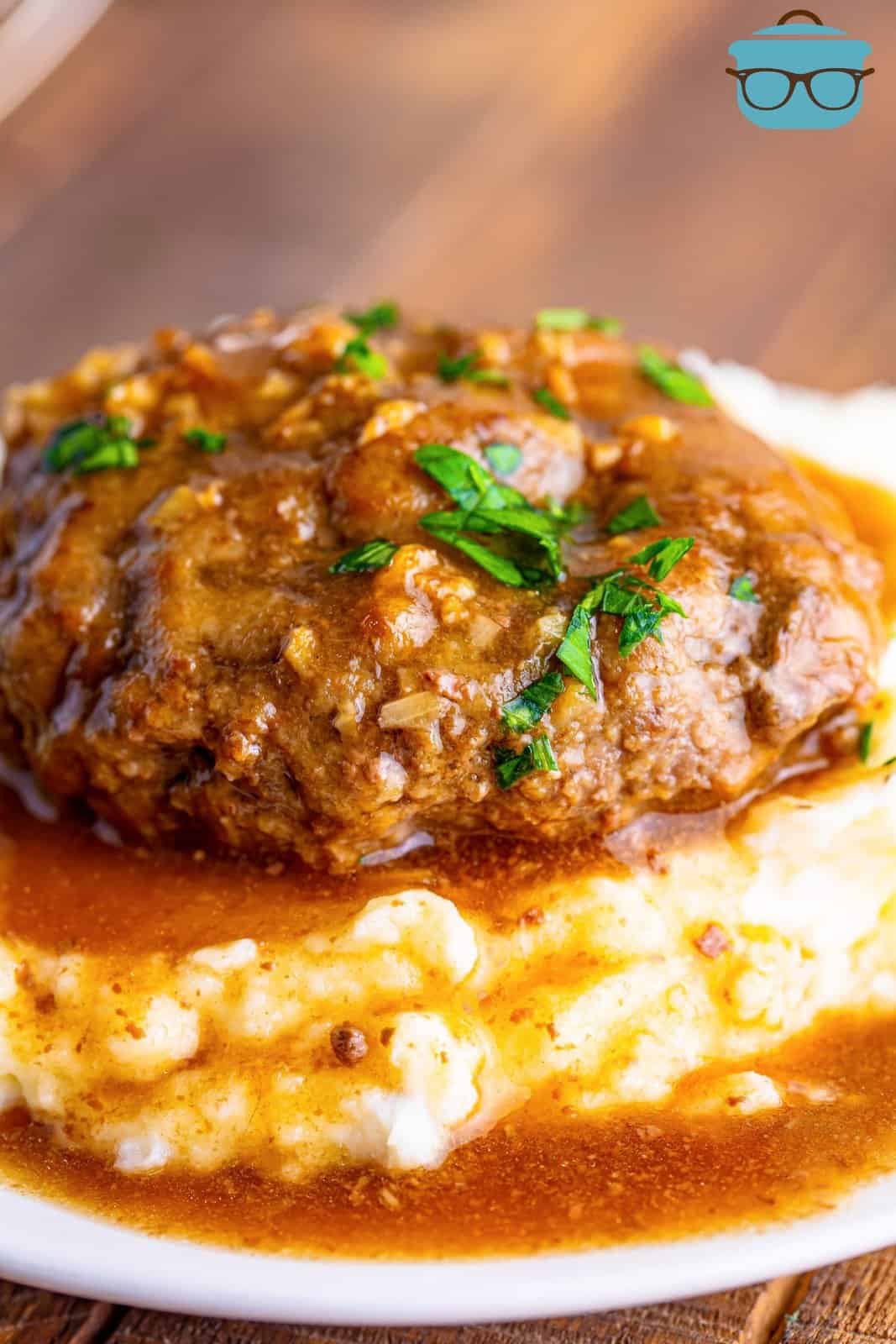 closeup photo of salisbury steak with gravy on cooked mashed potatoes on a white plate. 