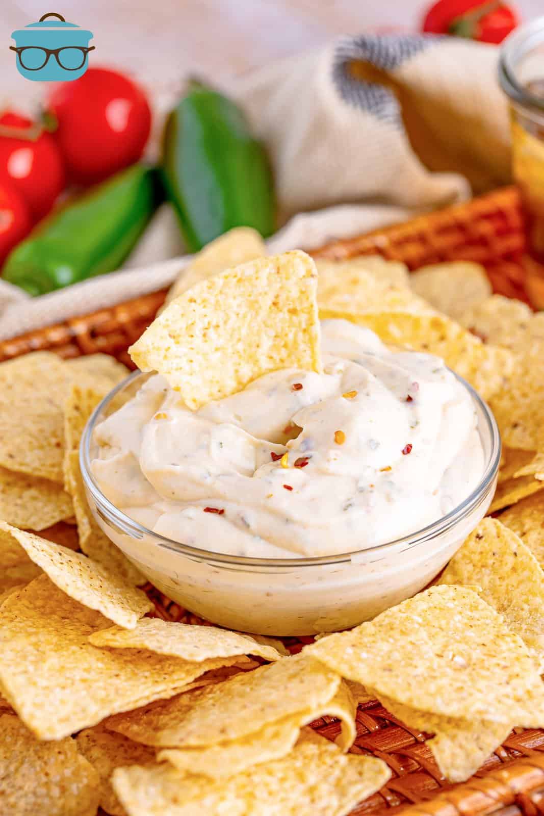 a tortilla chip shown dipped into the white sauce in a clear glass bowl.