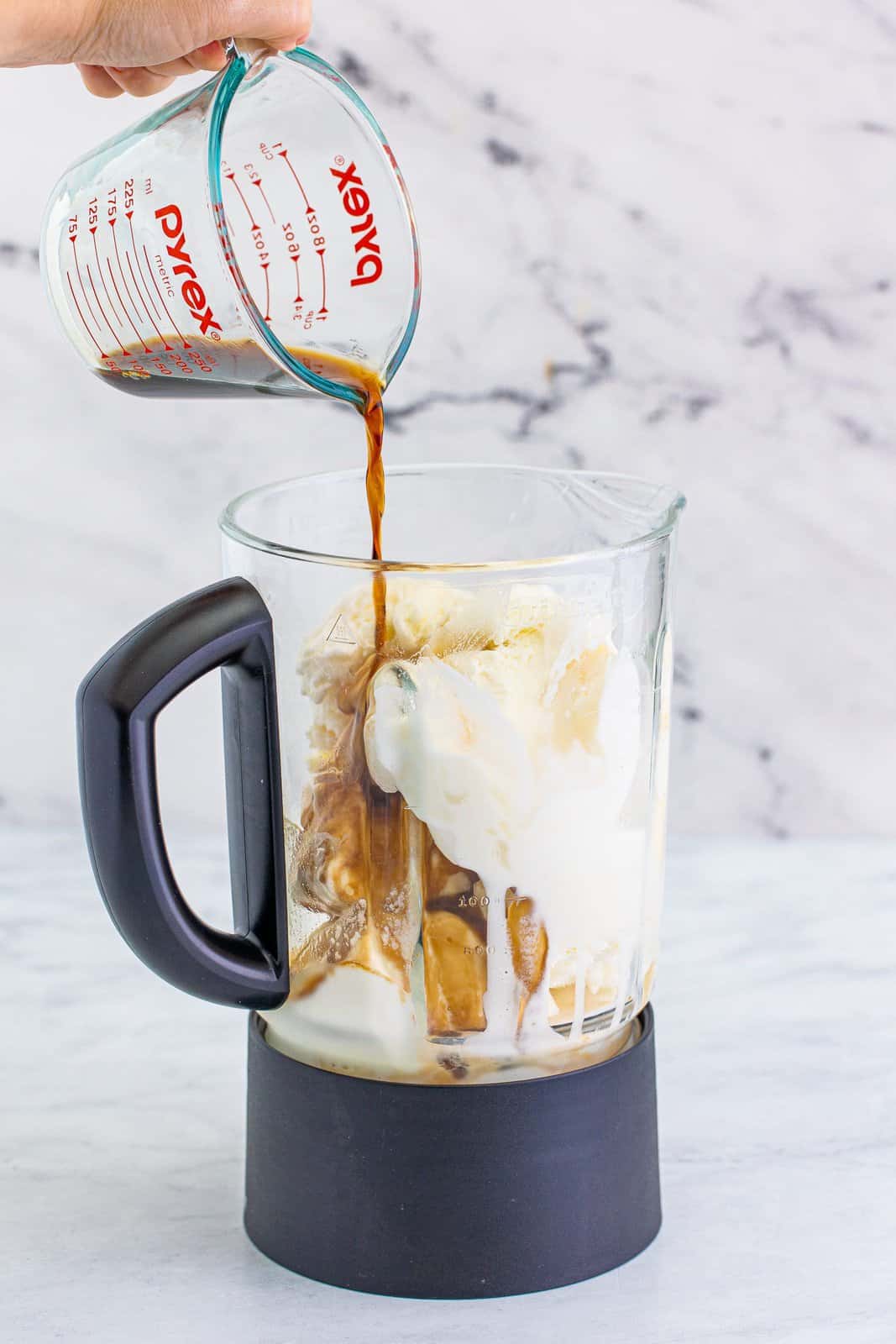pouring coffee liqueur into a blender with ice cream in it. 