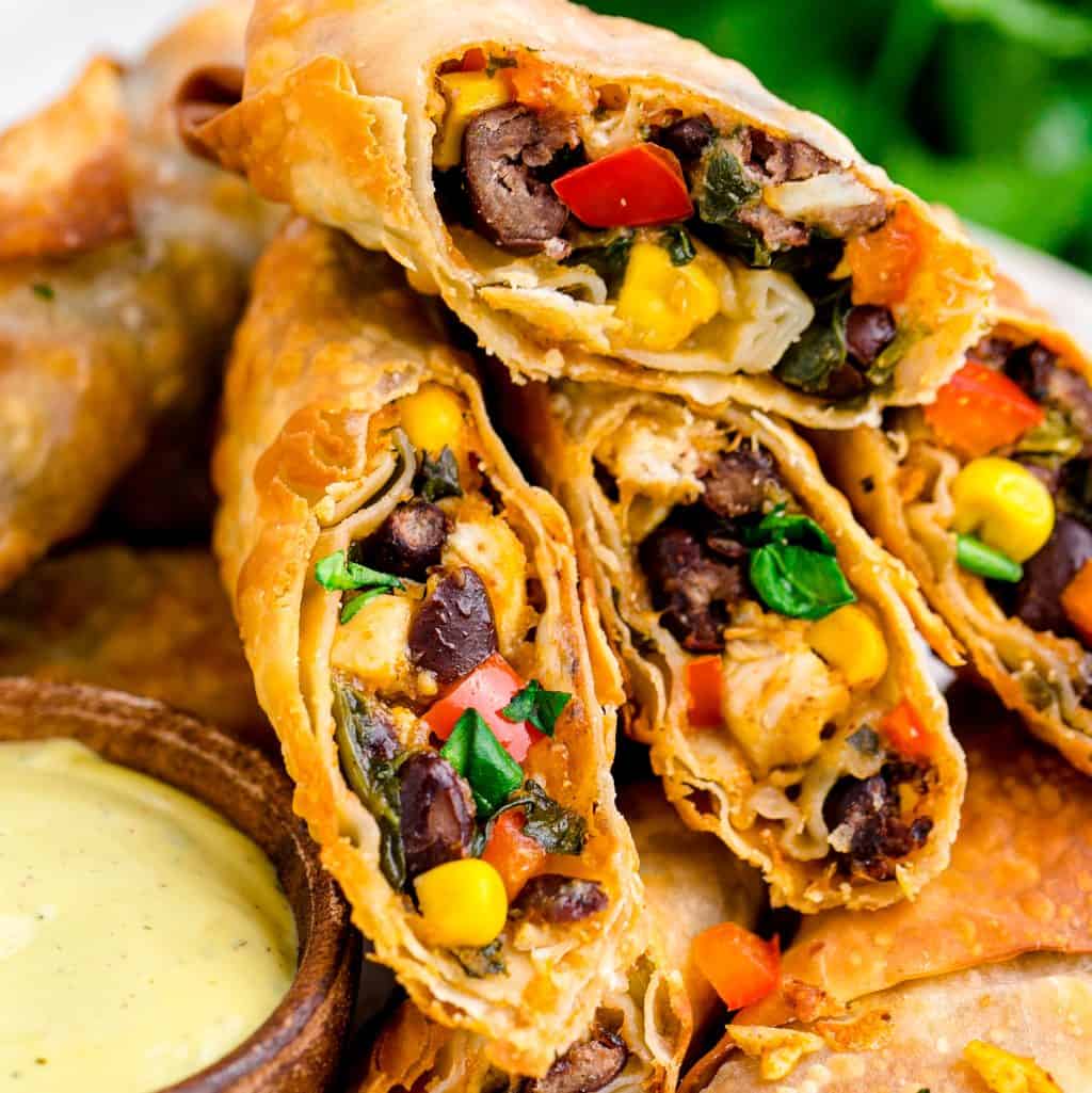 A close up shot of open egg rolls with peppers, corn, beans, and more inside of the wrapper.