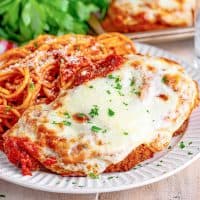A plate of chicken parmesan and spaghetti with tomato sauce.