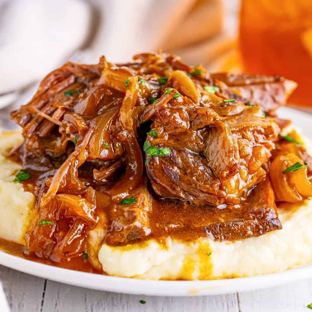 A plate of mashed potatoes covered with French Onion Pot Roast and sauce on top.