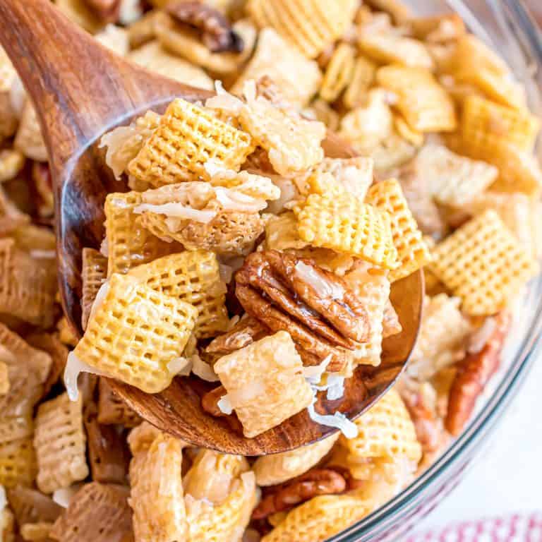 Close up square image of Sweet Holiday Chex Mix being held up with wooden spoon.