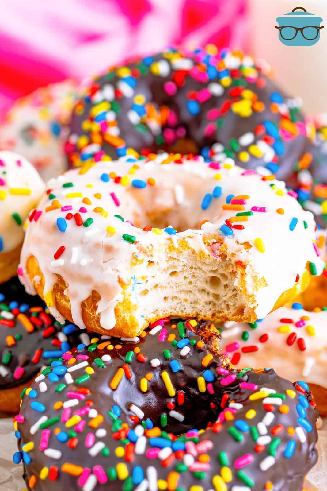 A vanilla frosted donut with a bite taken out surrounded by a few other chocolate frosted donuts. 