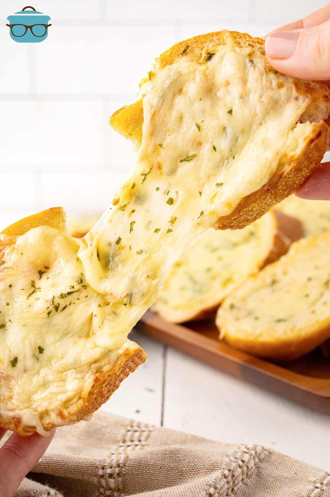 A hand separating a garlic cheesy slice of bread.