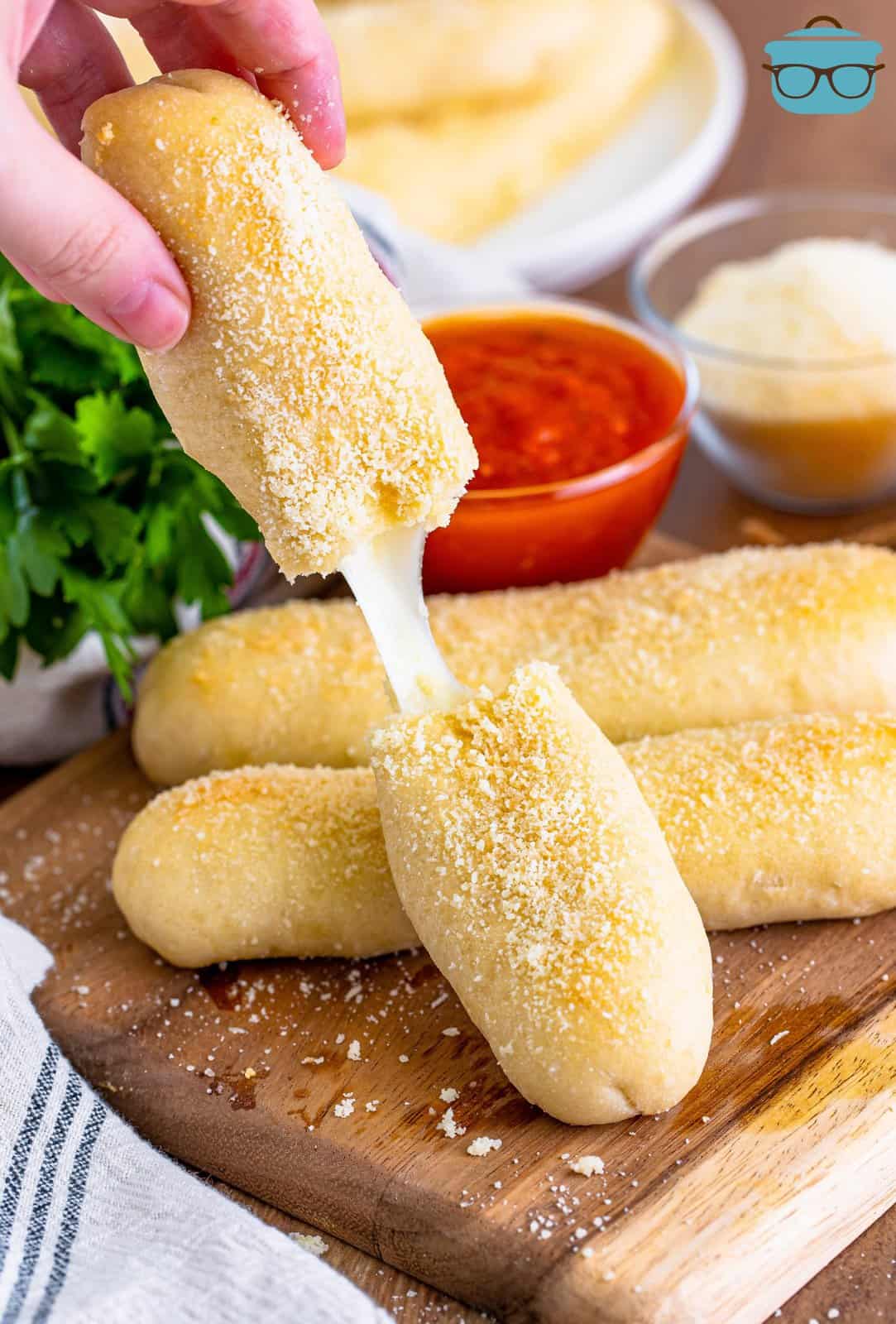 Fingers holding a broken open Bosco stick with mozzarella string cheese hanging between the two pieces.