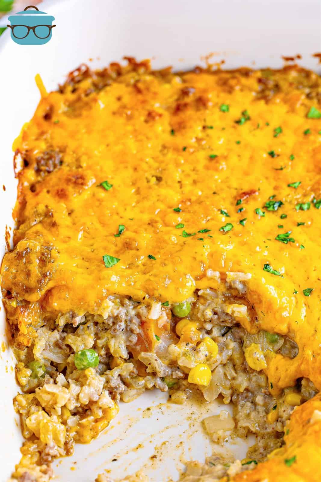A baking dish with a cheesy ground beef and rice casserole with a scoop taken out of it.