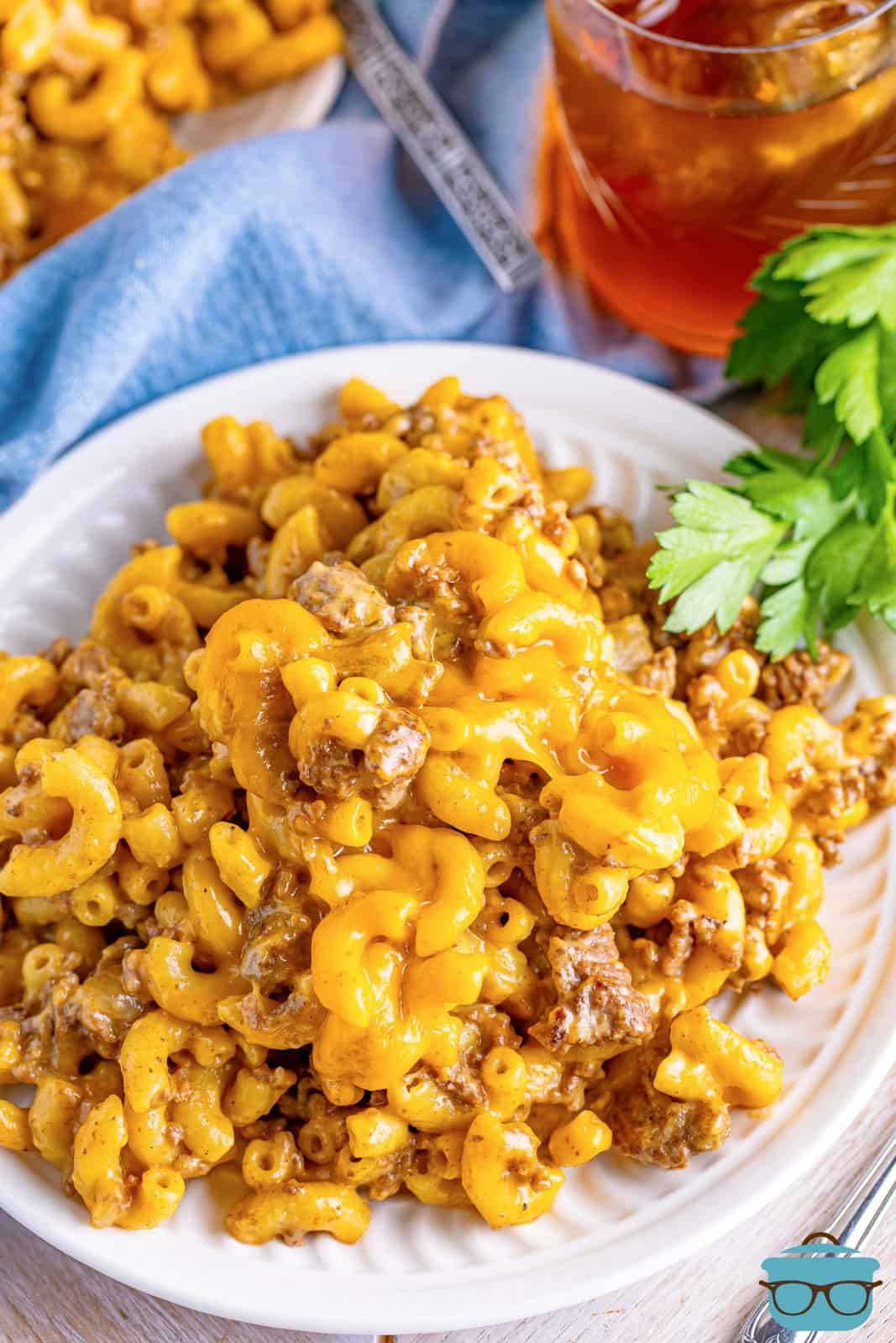 A plate of cheeseburger macaroni and some a glass of drink on the side.