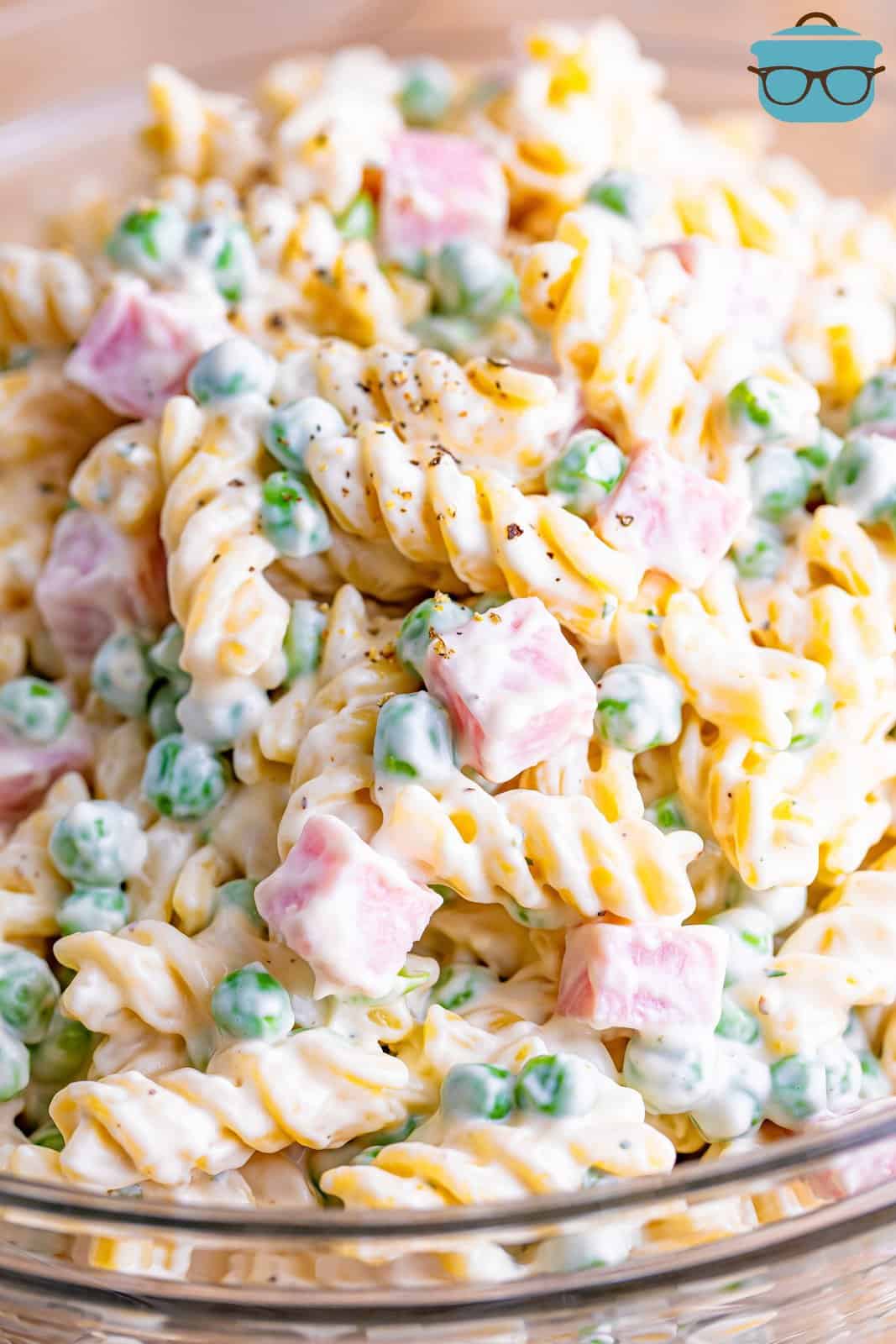 A close up of a pasta salad with pasta, peas, and ham.