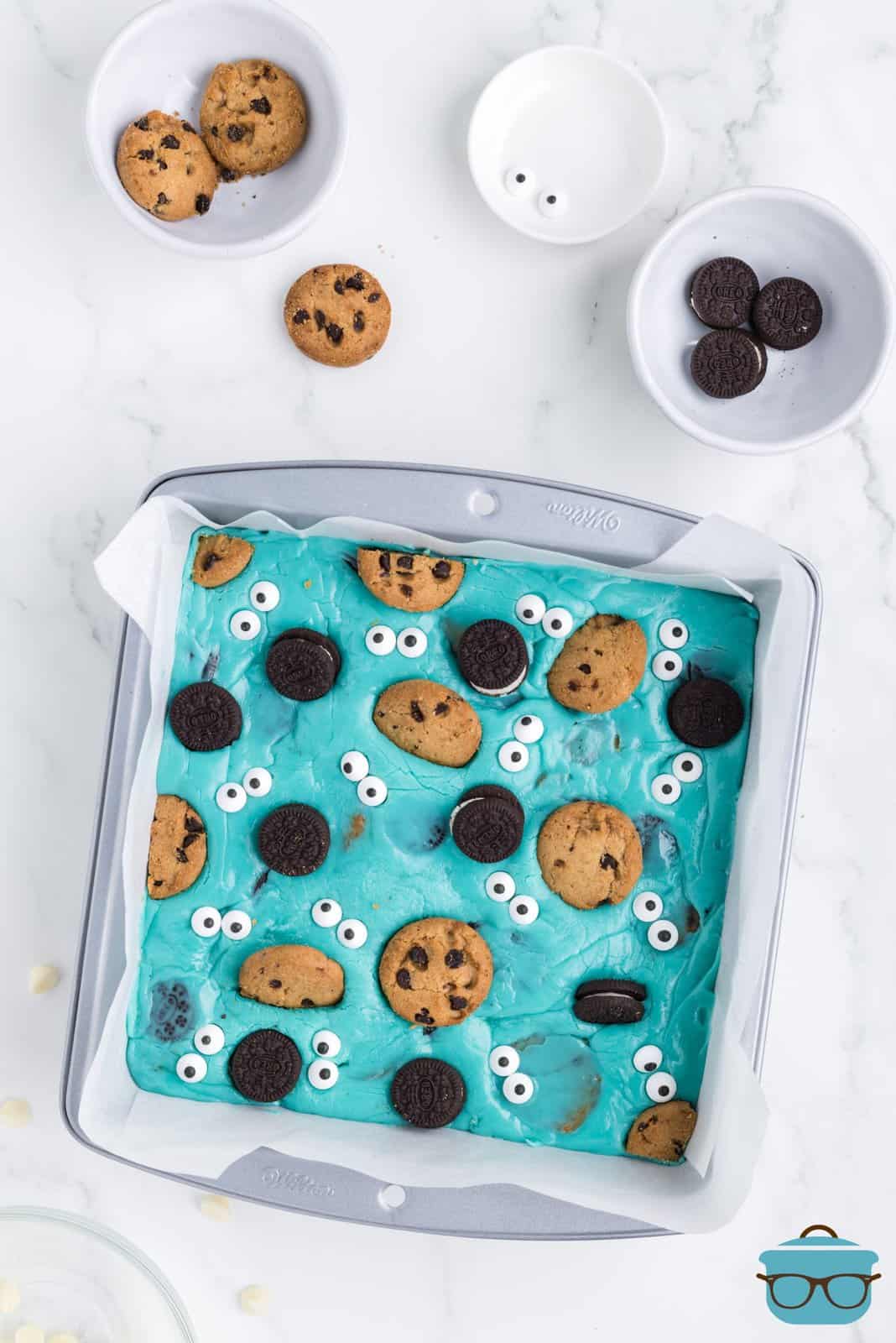 Blue fudge in a pan with cookies and candy eyes on top.
