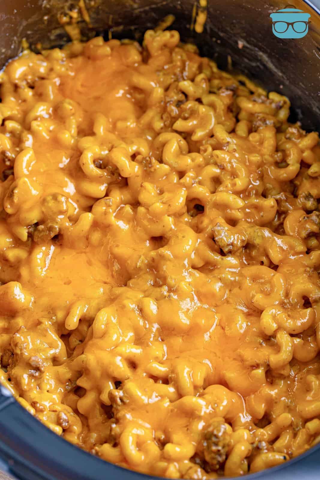 A Slow Cooker insert filled with Cheeseburger Macaroni with cheese on top.