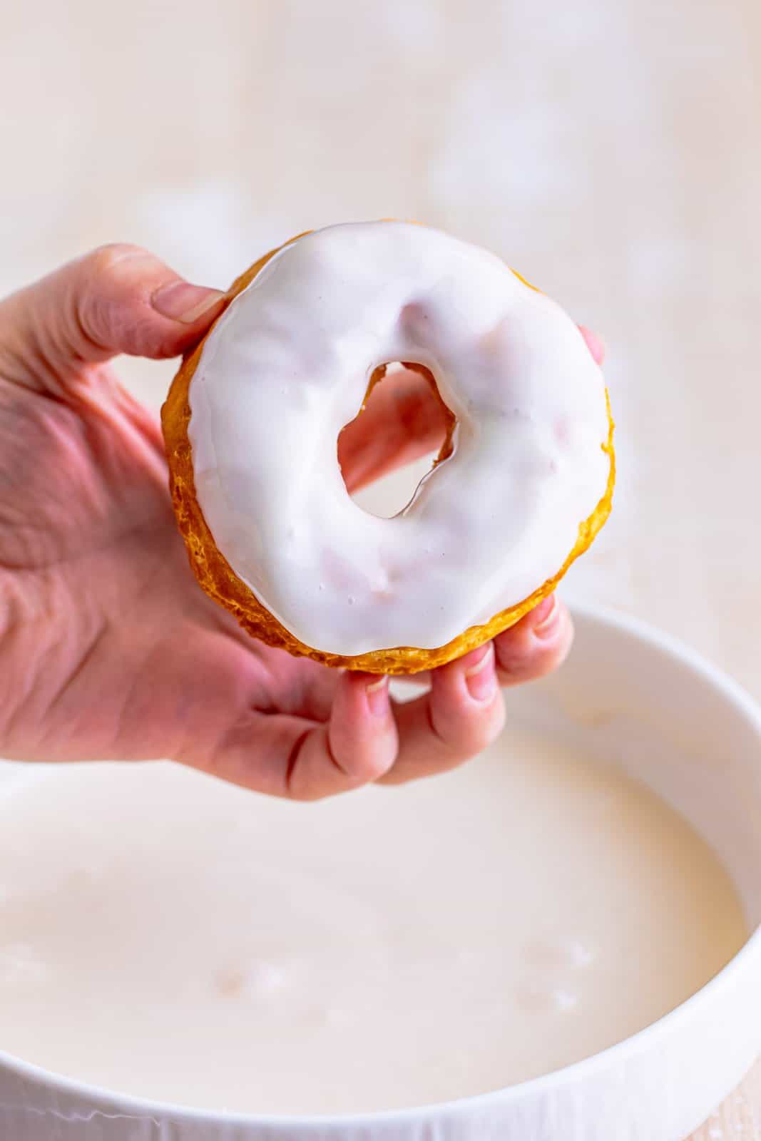 A hand holding a vanilla glazed donut.