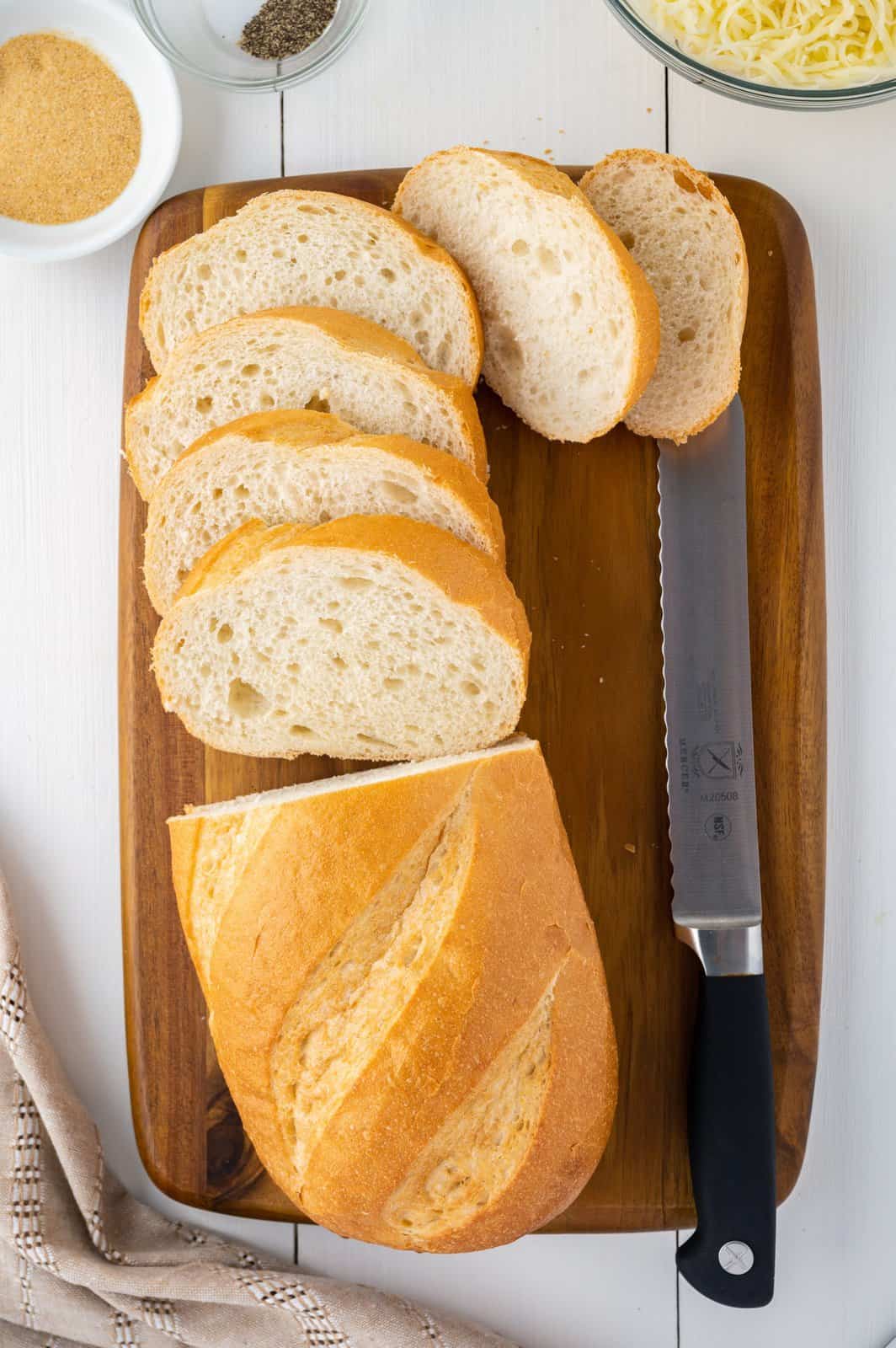 A cutting board with a half sliced loaf of bread and a bread knife.