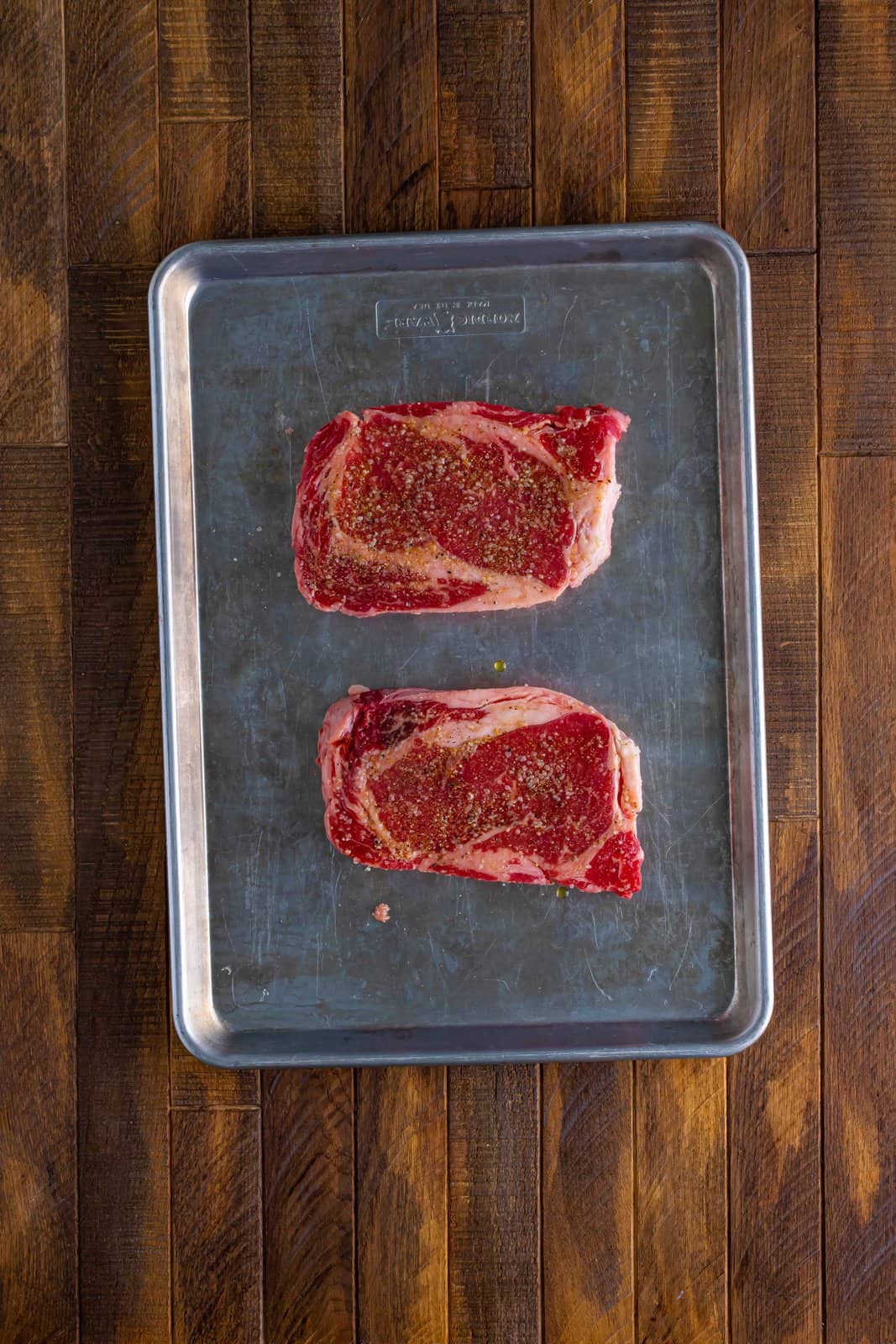 Two Ribeye steaks on a sheet pan.