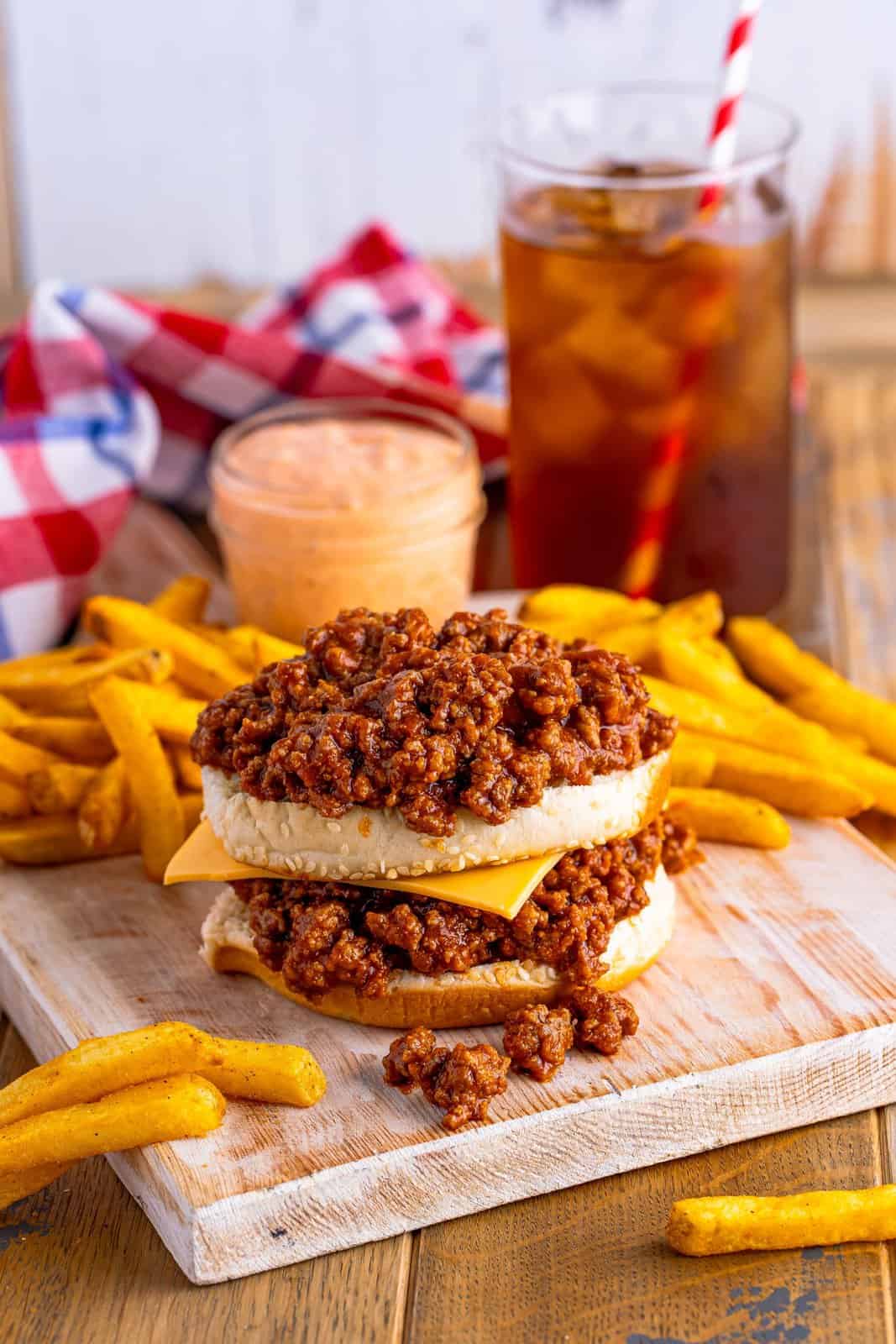Part of a sloppy joe made with meat, sesame seed bottom buns, and cheese.