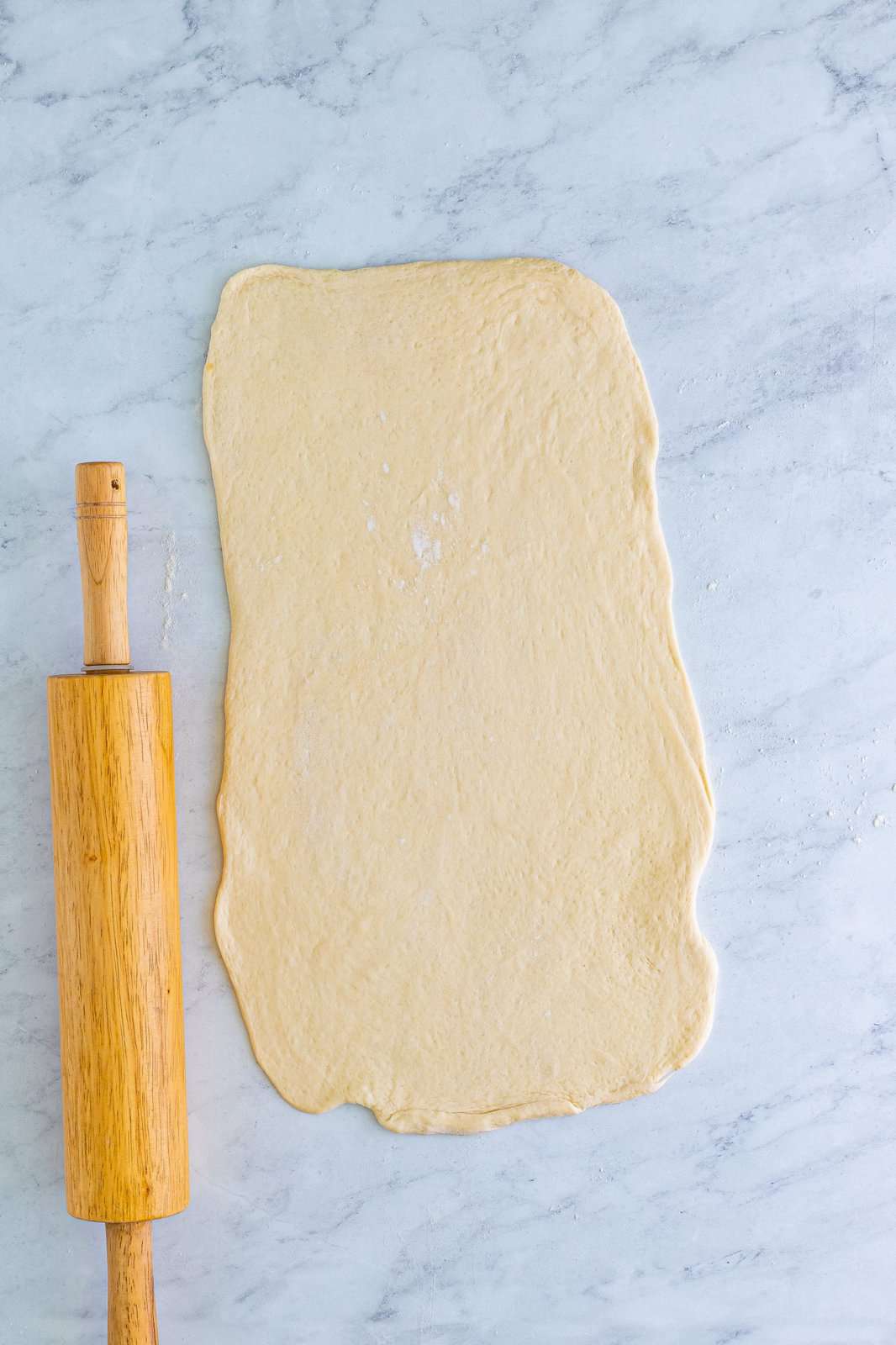 A rolling pin next to a rolled out piece of pizza dough.