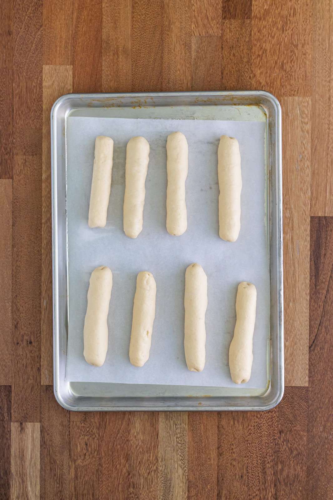 A baking sheet lined with parchment paper and Bosco sticks rolled up covered in dough.