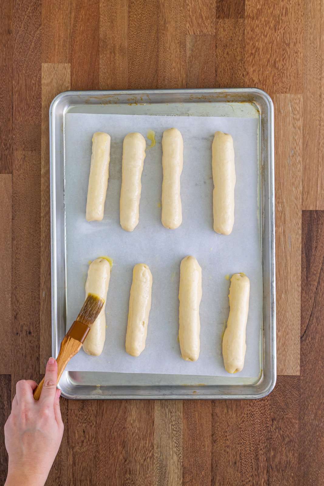 A pastry brush brushing butter on top of the bosco sticks.`