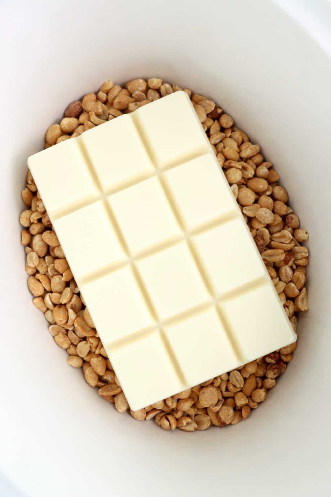 A slow cooker insert with roasted peanuts on the bottom and almond bark on top.
