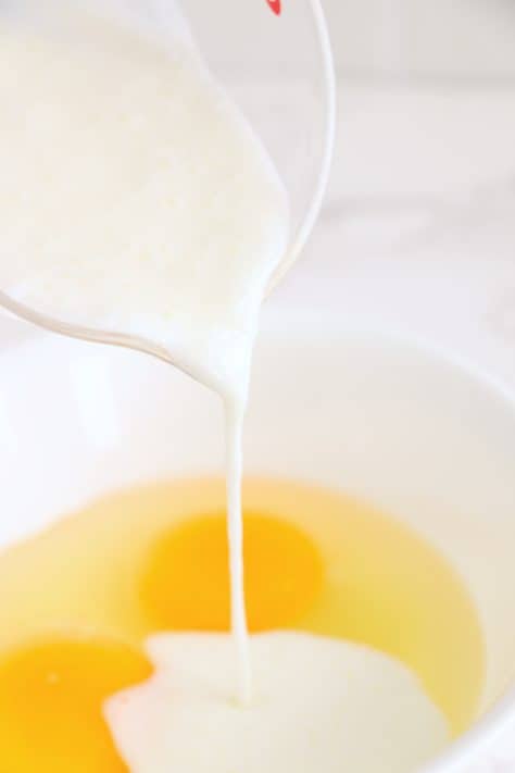 A mixing bowl with eggs and buttermilk being poured in.