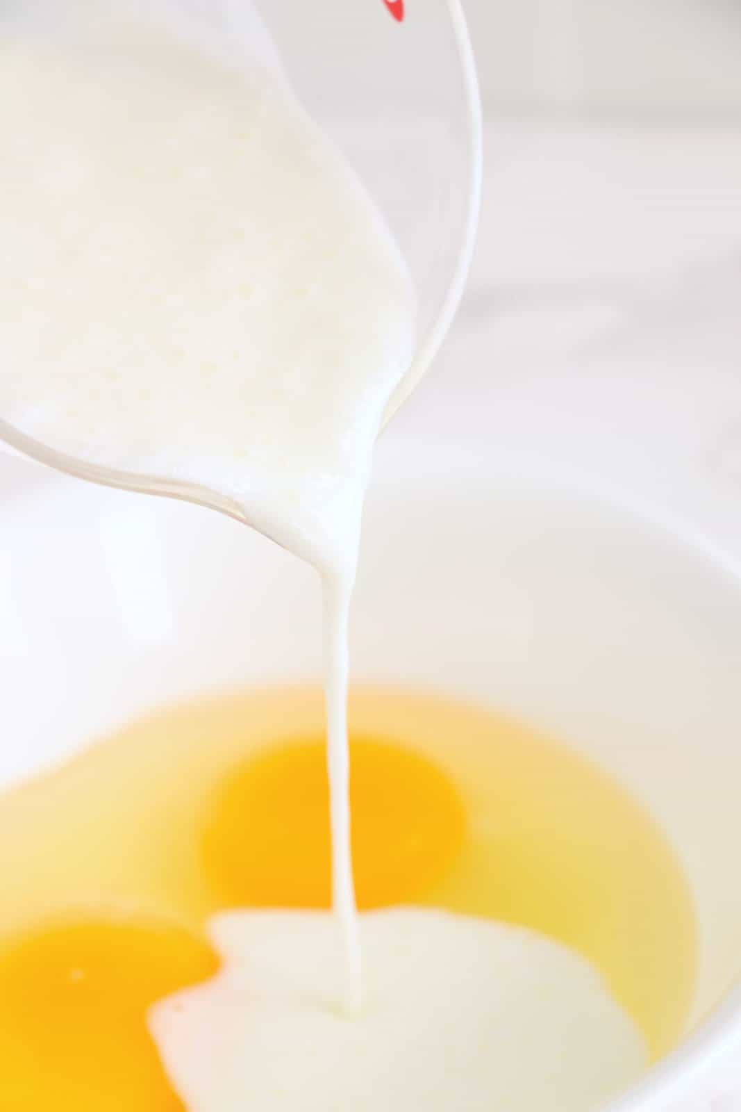 A mixing bowl with eggs and buttermilk being poured in.