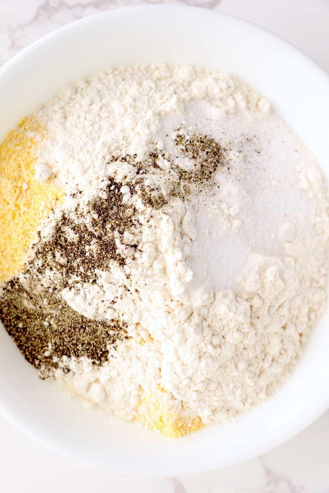 A mixing bowl with flour, garlic powder, cornmeal, parmesan cheese, salt and pepper.