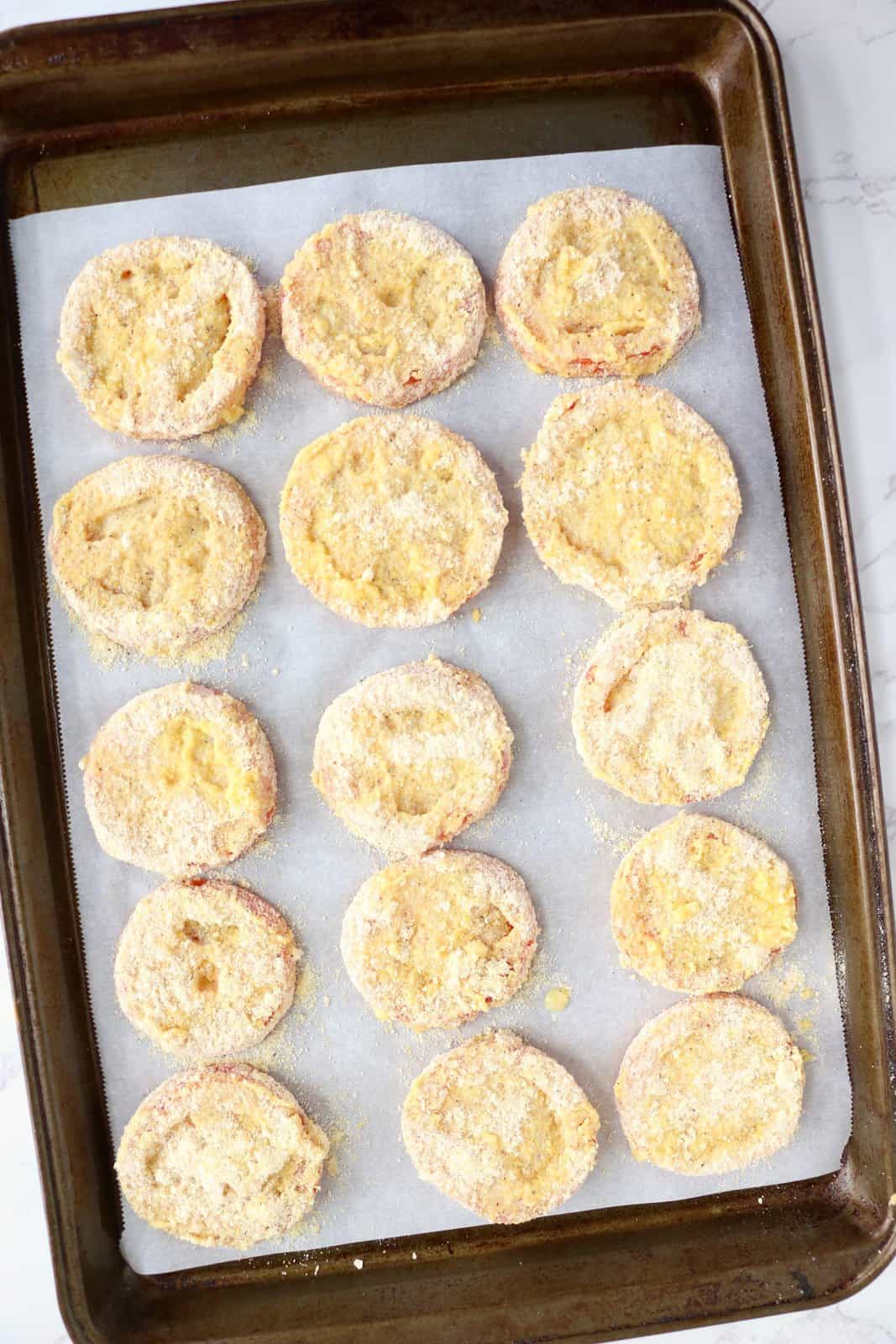A baking sheet lined with parchment paper and breaded tomatoes on top.
