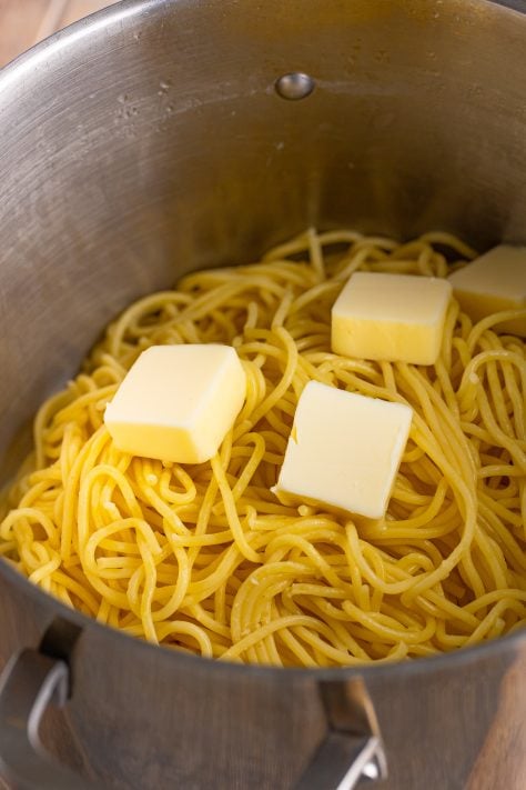 Spaghetti with butter chunks in a pot.