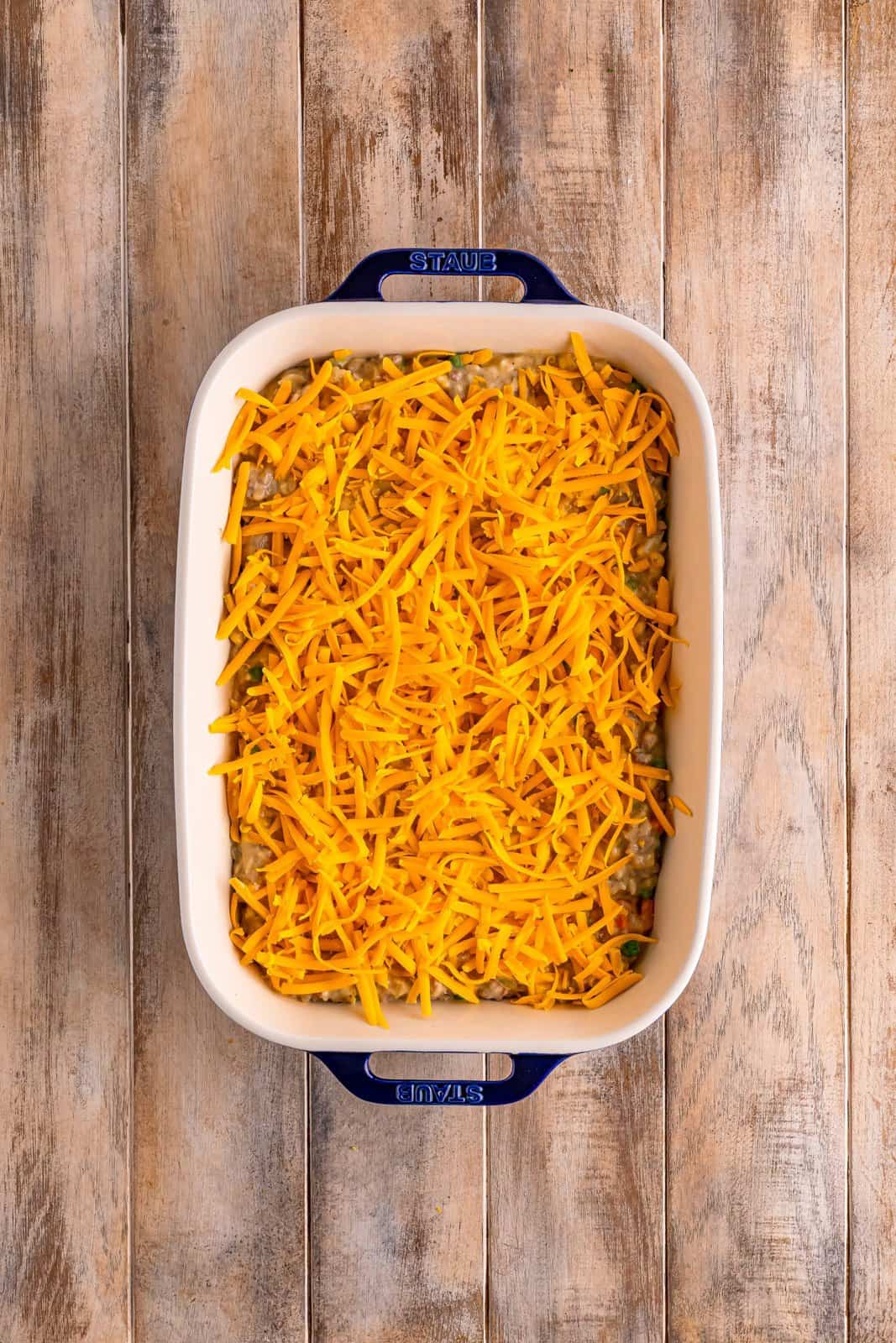 A casserole dish with a ground beef and rice casserole in it covered with shredded cheese.