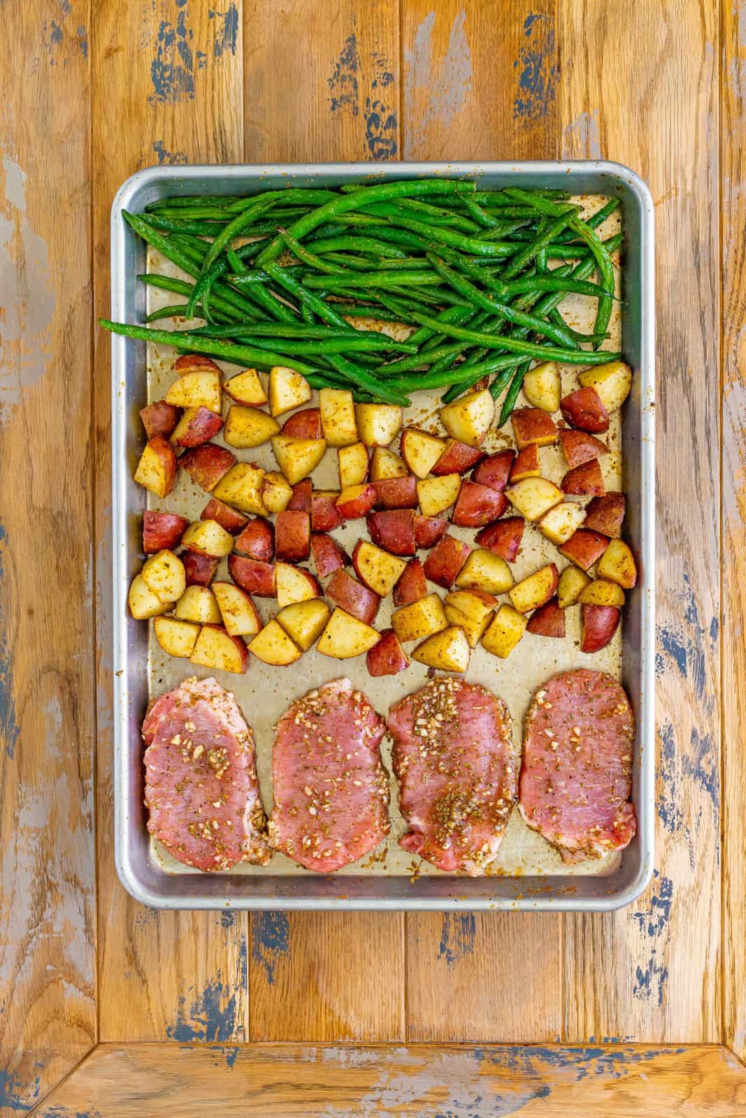 A sheet pan with seasoned pork chops and green beans and potatoes.