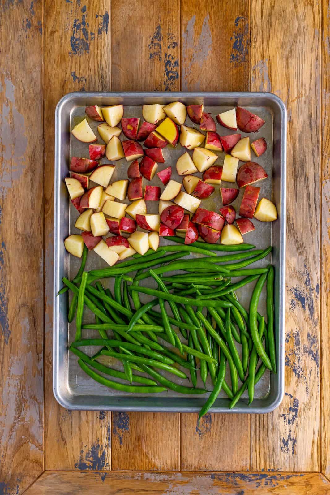 A sheet pan with green beans on half and cut up potatoes on the other.