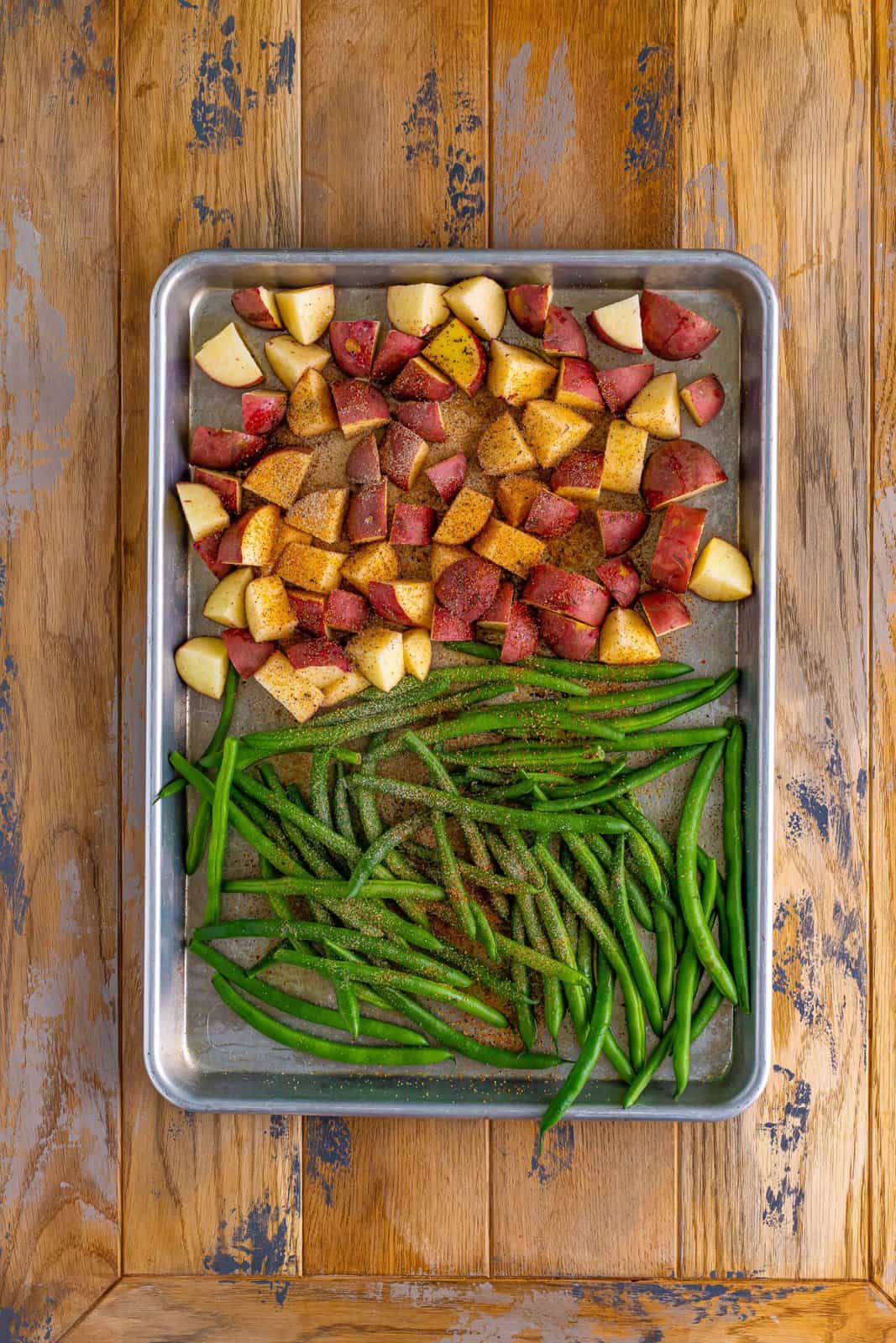 Sheet pan with green beans, potatoes, and herbs and spices. 