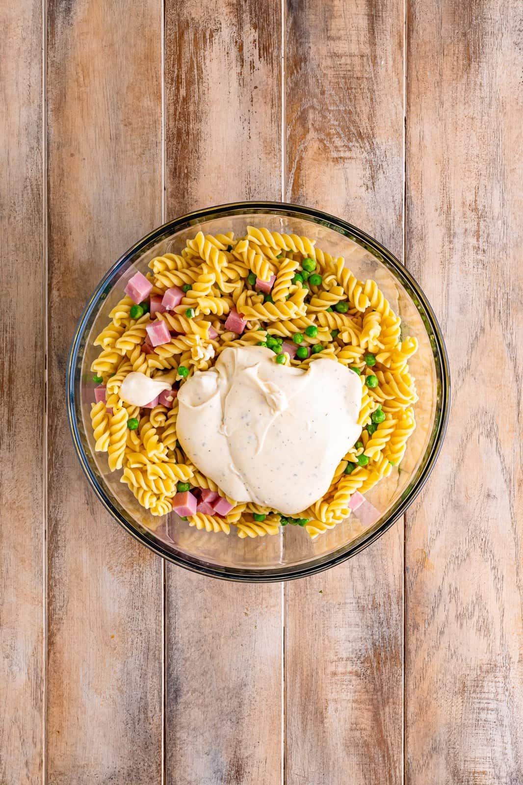 A bowl of rotini pasta, ham, peas, and mayo based dressing.