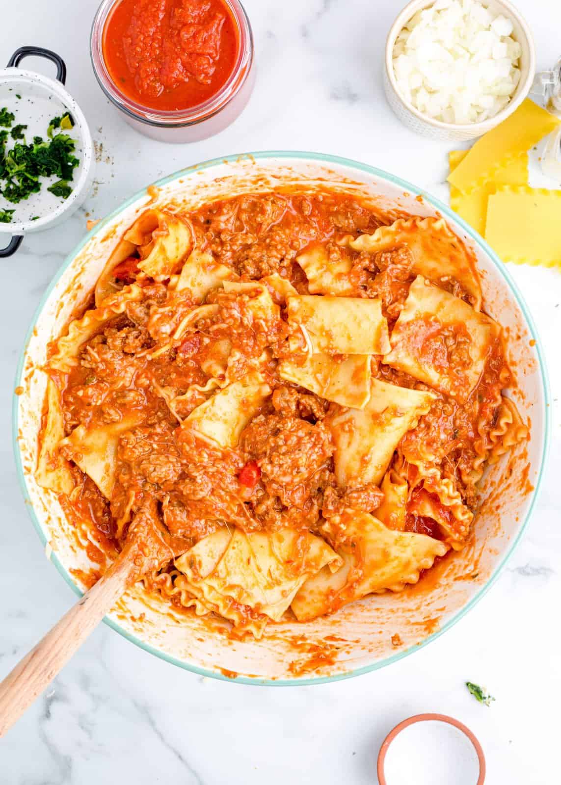 A skillet with lasagna noodles, marinara sauce, ground beef, onion , and other lasagna ingredients.