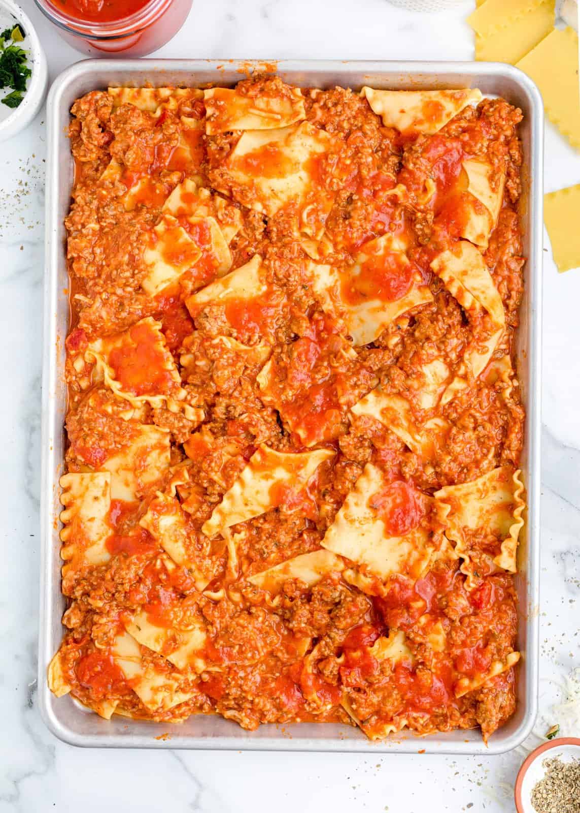 A sheet pan with lasagna noodles, ground beef mixture and marinara sauce all spread out. 