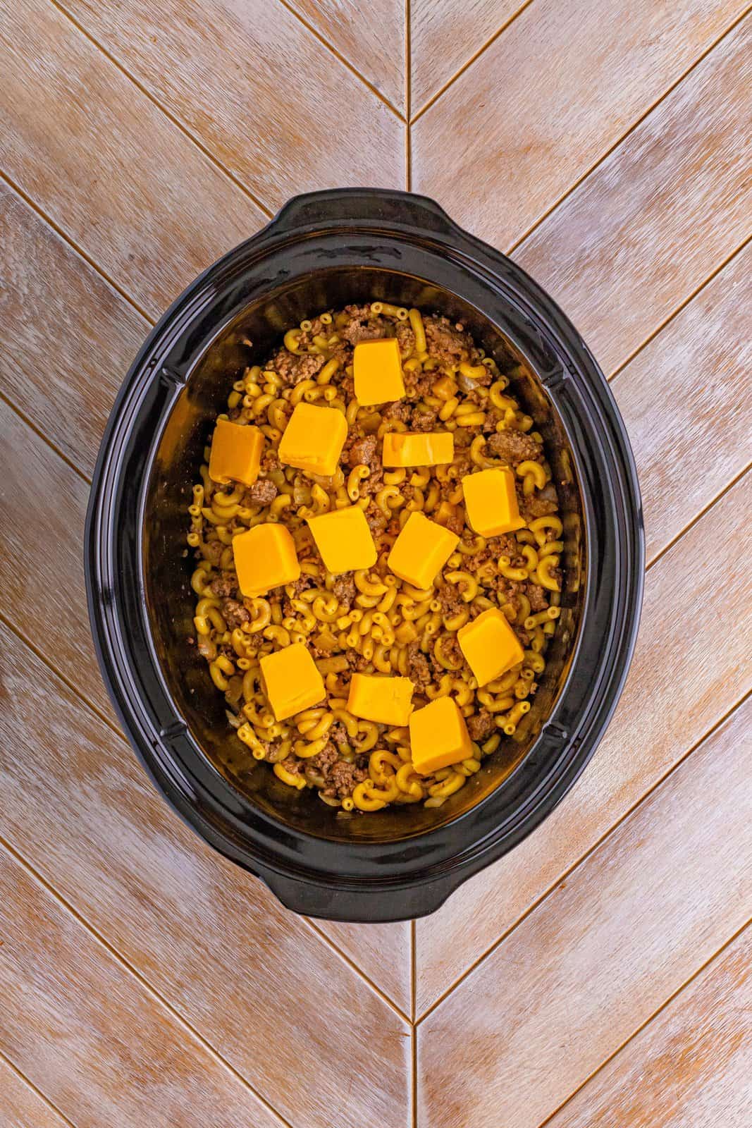 Cubed up Velveeta cheese on top of food in a crockpot.