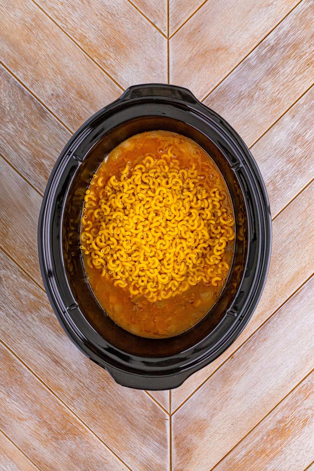 A Slow Cooker with macaroni on top of other ingredients.