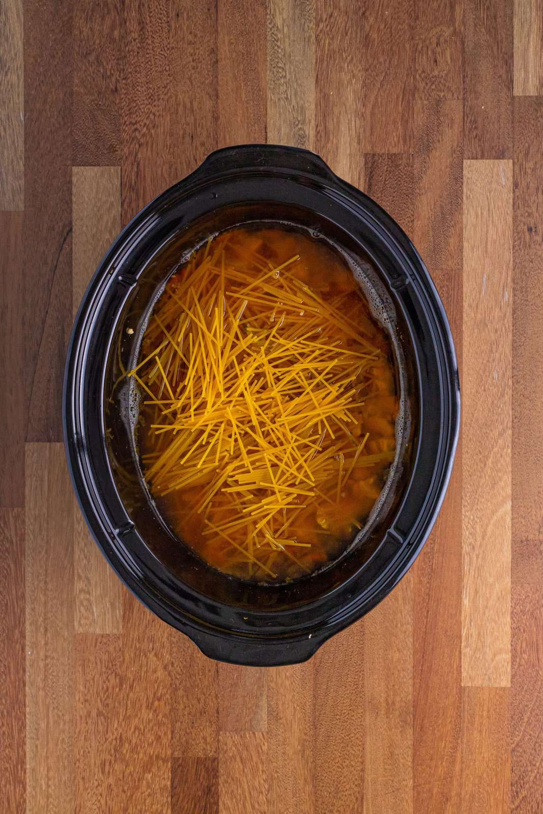 Broken up spaghetti pasta on top of soup in Crockpot.