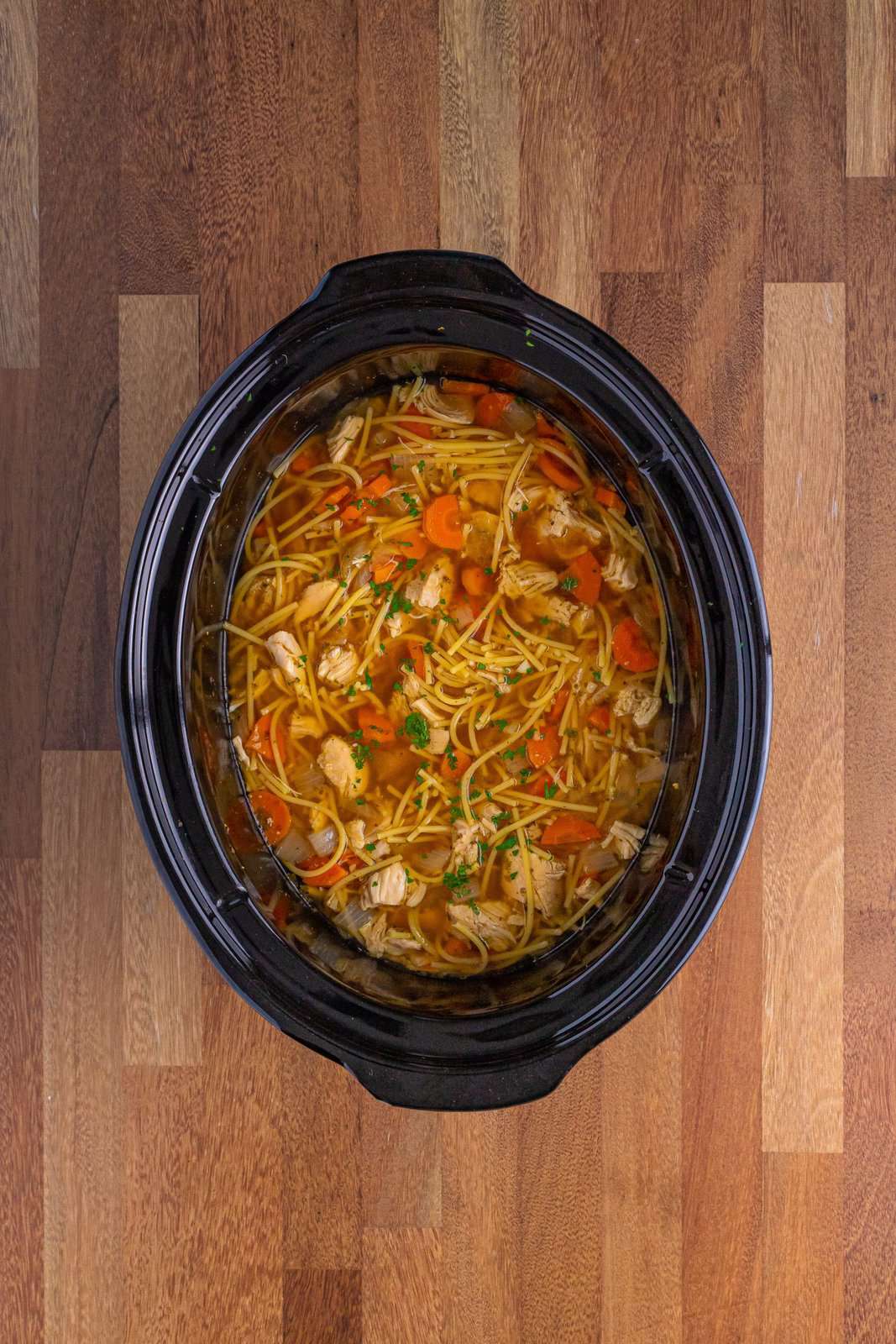 A Slow Cooker with completed Chicken Noodle Soup using spaghetti.